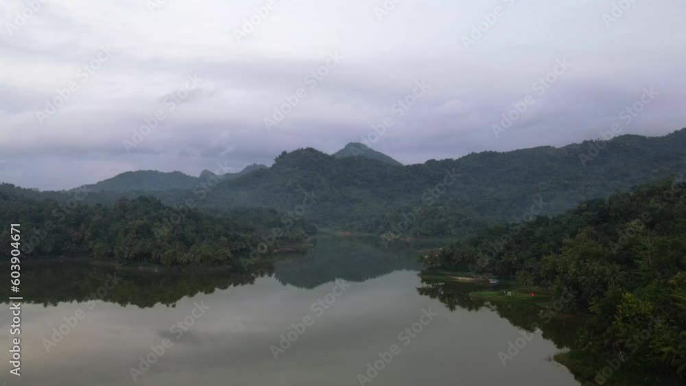 Aerial forward flight over lake with green hills in background during cloudy day Aerial forward flight over lake with green hills in background during cloudy day