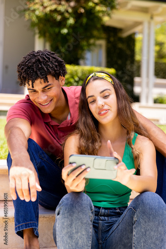 Smiling biracial young woman taking selfie with boyfriend while sitting on steps outside house