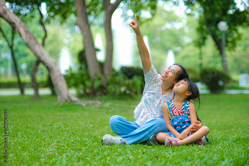 Mother and little daughter sitting on the grass together in the park. Mother having fun with her little daughter outdoors in green nature park. Happy family concept. Mother's Day