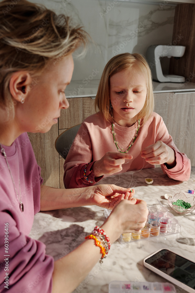 Mature Caucasian woman and her daughter spending weekend together at home creating accessories with beads