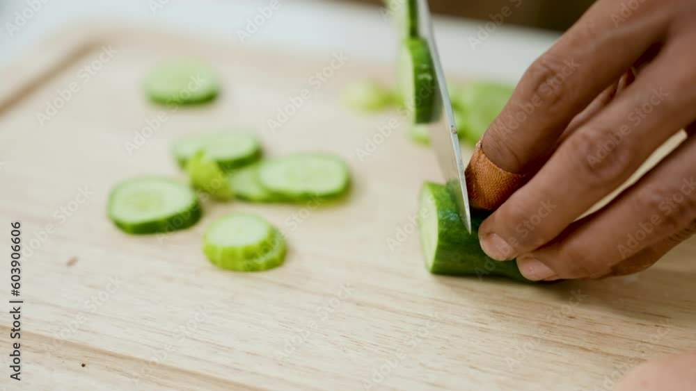 Close-up cucumber being touched by hand young Asian man on cutting board, circular knife, chef is chopping vegetables prepare ingredients, cook for yourself on holidays that do not want leave house. Close-up cucumber being touched by hand young Asian man on cutting board, circular knife, chef is chopping vegetables prepare ingredients, cook for yourself on holidays that do not want leave house.