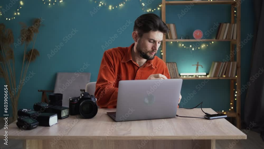 Photographer working on a laptop at the workplace sends captured images ...