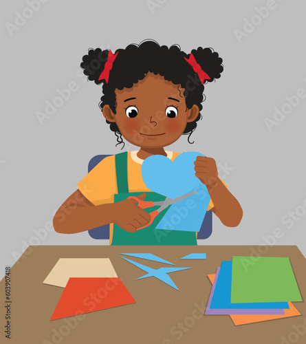 Cute little African girl cutting colored paper with scissors making heart shape paper cut art craft
