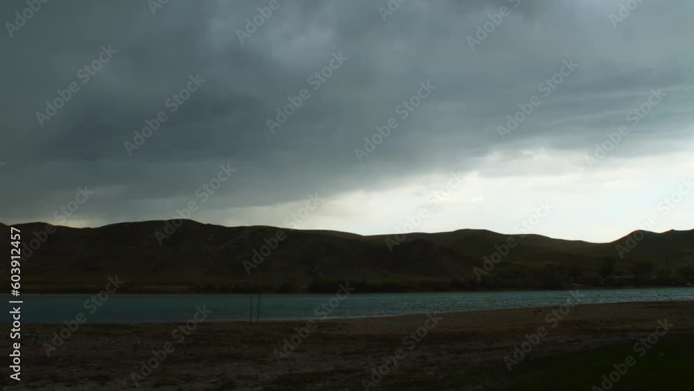 Captivating time-lapse Summer rainstorm over the fast-flowing river with majestic mountains, creating a dusty and arid atmosphere. Dark Sky, moody feeling. Captivating time-lapse Summer rainstorm over the fast-flowing river with majestic mountains, creating a dusty and arid atmosphere. Dark Sky, moody feeling.