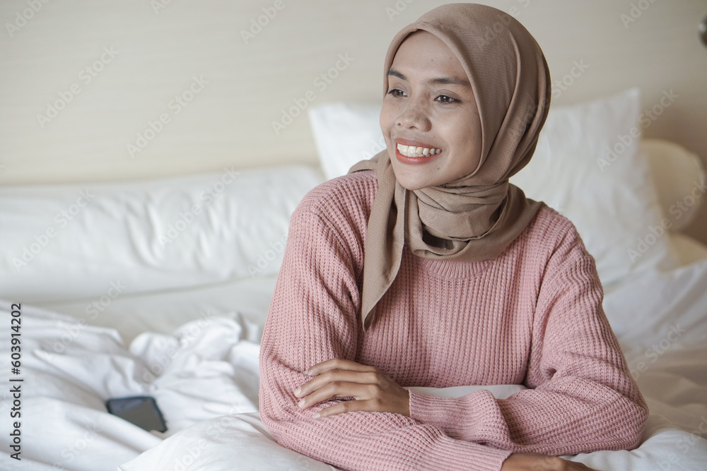 Portrait of a beautiful young Asian Muslim woman wearing a headscarf on a bed on vacation at a hotel Portrait of a beautiful young Asian Muslim woman wearing a headscarf on a bed on vacation at a hotel