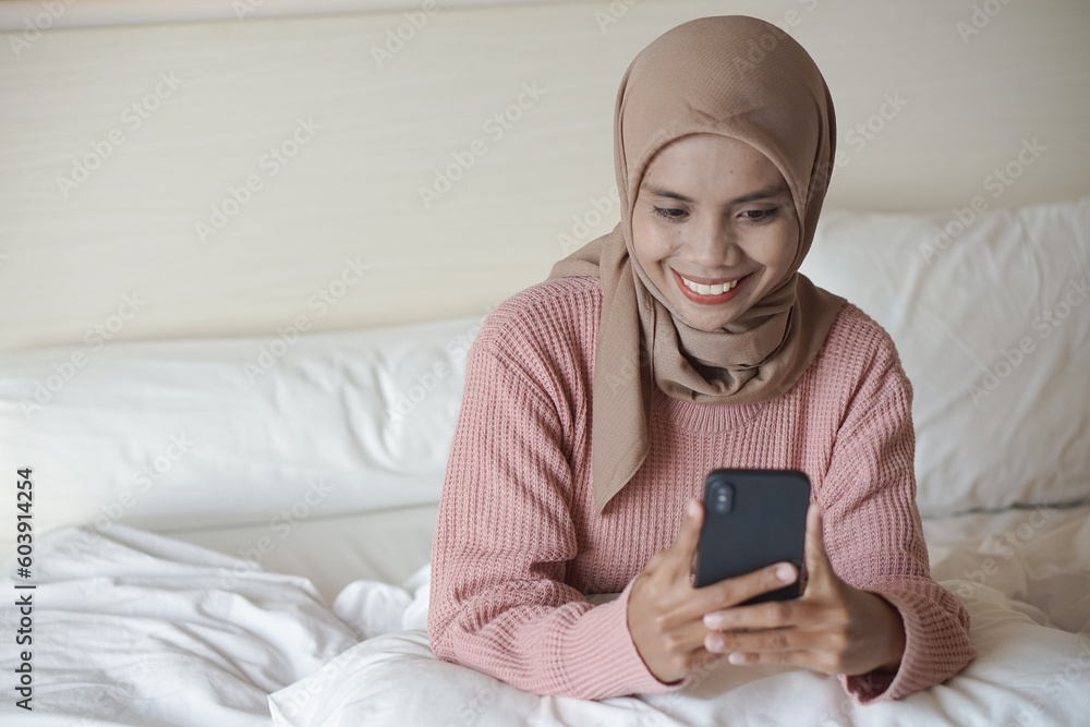 Portrait of a beautiful young Asian Muslim woman wearing a headscarf laying down while holding a mobile phone Portrait of a beautiful young Asian Muslim woman wearing a headscarf laying down while holding a mobile phone