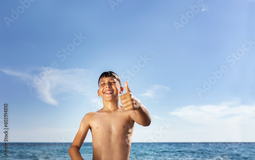 A nine-year-old boy is depicted at the beach, completely soaked. His brown hair is wet, sticking to his face as water droplets trickle down.