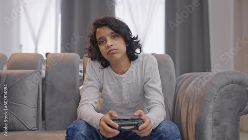Bored Indian kid boy playing video games on controller