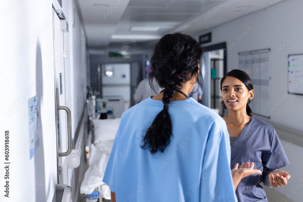 Two biracial female doctors wearing scrubs, talking in corridor at hospital Two biracial female doctors wearing scrubs, talking in corridor at hospital
