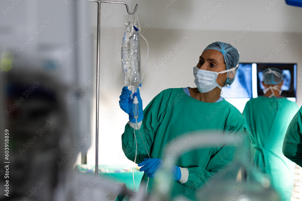 © Wavebreak Media - Biracial female surgeon inspecting drip bag in operating theatre at hospital