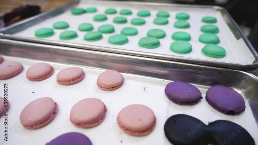 Dozens of freshly baked colorful macaron cookies, green pink purple french meringue cookie shells, close up 4K Dozens of freshly baked colorful macaron cookies, green pink purple french meringue cookie shells, close up 4K