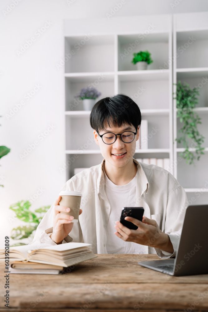 Happy student male using laptop computer, mobile phone, working freelance project online, sitting outdoors. Successful business. Asian student studying, learning language, online education concept Happy student male using laptop computer, mobile phone, working freelance project online, sitting outdoors. Successful business. Asian student studying, learning language, online education concept