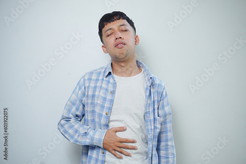Worried facial expression of Asian man who got problem with stomach isolated on white background photo