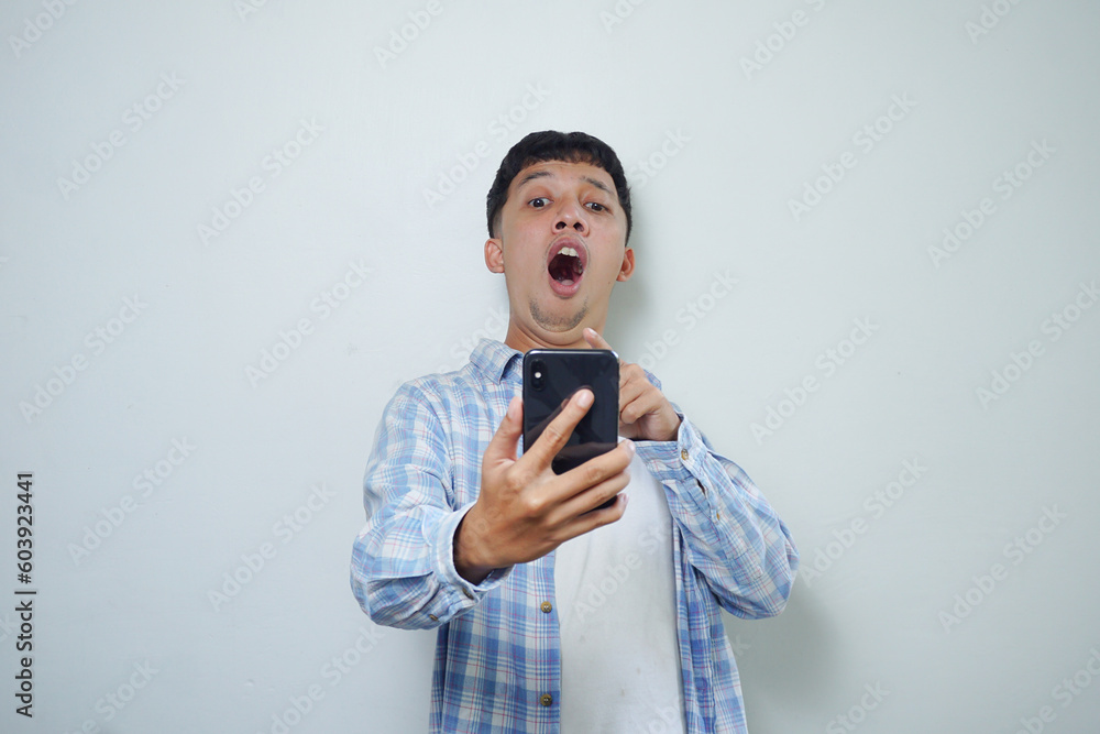 facial expression of very shocked asian man using mobile phone isolated on white background facial expression of very shocked asian man using mobile phone isolated on white background