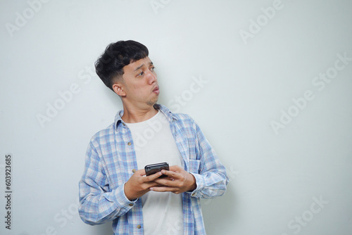 asian man facial expression looking sideways while holding mobile phone isolated on white background photo