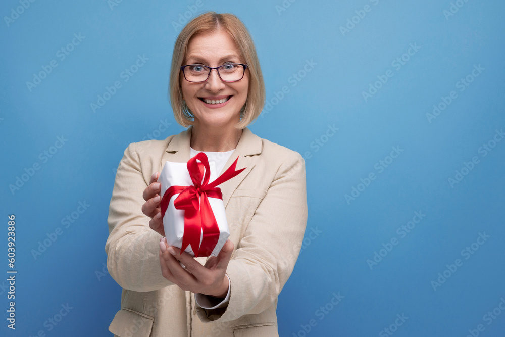 middle-aged business concept. 50s woman in a jacket with a gift on a studio background with copy space middle-aged business concept. 50s woman in a jacket with a gift on a studio background with copy space