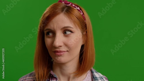 Portrait of funny young woman rolling eyes spontaniously then looking at camera on green color background. Woman grimacing childishly on camera. Emotional expressions concept. photo