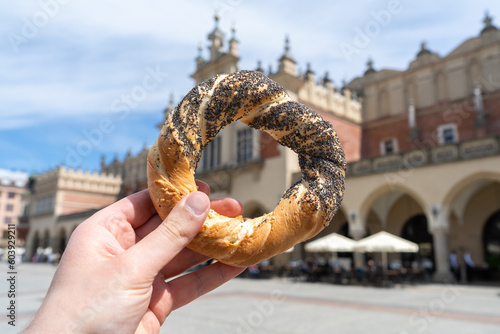 Hand holding obwarzanek krakowski pretzel on Kraków Main Market Square, with Cracow Cloth Hall Sukiennice in background. Krakowskie obwarzanki, traditional polish snack in Krakow, Poland.