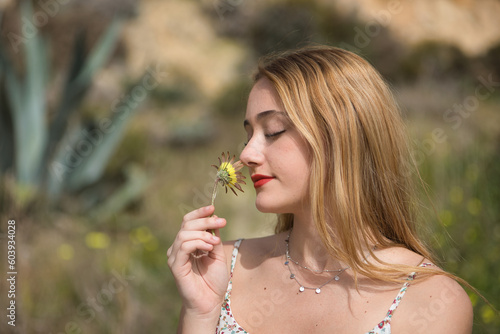 Young woman, blonde and beautiful, with closed eyes smelling a yellow daisy. Spring concept, flowers, nature.