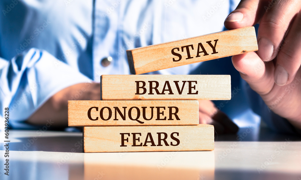 Close up on businessman holding a wooden block with "Stay brave. Conquer fears" message - obrazy, fototapety, plakaty 