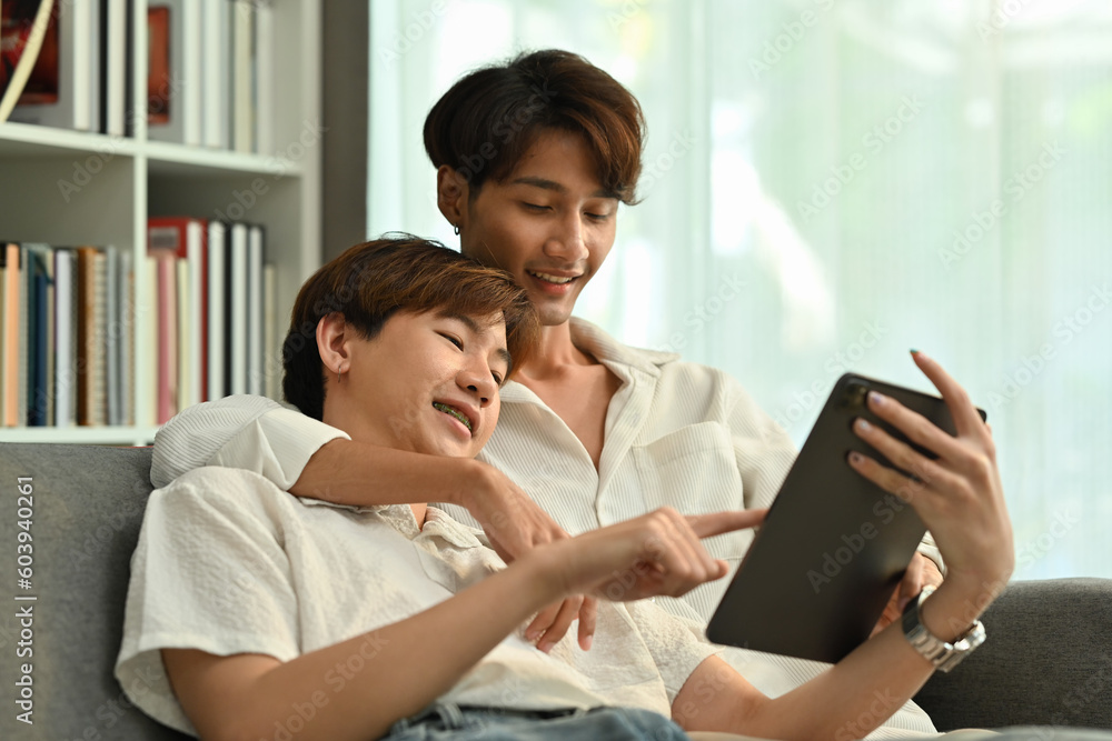 Passionate homosexual couple relaxing on couch and browsing internet on digital tablet. LGBT, love and lifestyle concept Passionate homosexual couple relaxing on couch and browsing internet on digital tablet. LGBT, love and lifestyle concept