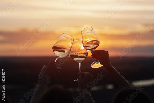 A group of girlfriends raise a toast with glasses of white wine on a sunset. Close shot.	
