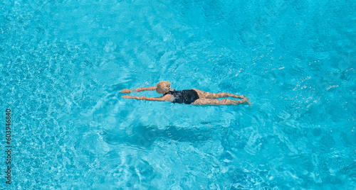 View from the height of the flight of a bird, a woman in a swimsuit swims in a blue pool, rests and relaxes