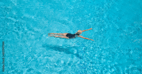 Zenith  a view from a height of an adult beautiful blonde woman in a black swimsuit swims in a blue pool  leisure and vacation time  a view of the pool with a swimming European woman