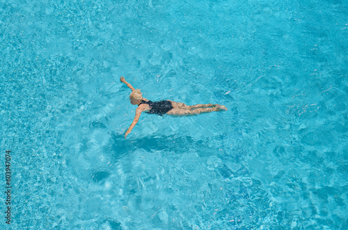 Adult beautiful woman in a black swimsuit swims in a blue pool, leisure and vacation time, bird's eye view of the pool, top view. © Ed