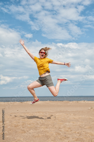 Cheerful young woman having fun and jumping on the sand