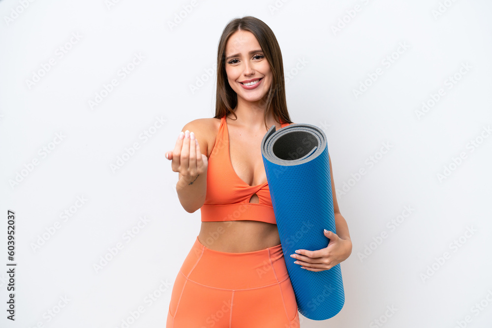 Young beautiful sport woman going to yoga classes while holding a mat isolated on white background inviting to come with hand. Happy that you came Young beautiful sport woman going to yoga classes while holding a mat isolated on white background inviting to come with hand. Happy that you came