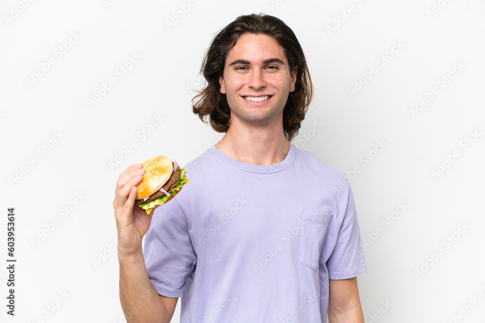 Young handsome man holding a burger isolated on white background smiling a lot Young handsome man holding a burger isolated on white background smiling a lot