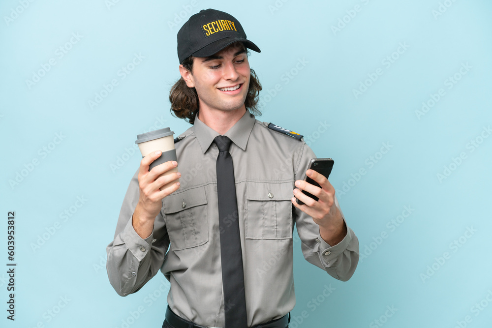 Young safeguard man isolated on blue background holding coffee to take away and a mobile Young safeguard man isolated on blue background holding coffee to take away and a mobile