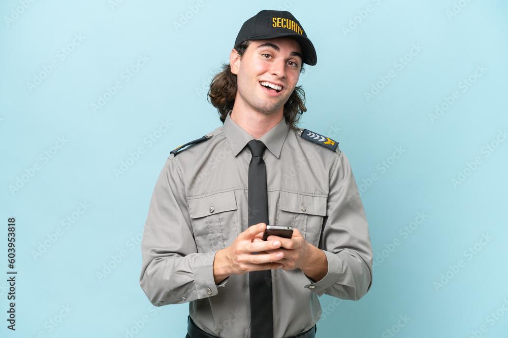 Young safeguard man isolated on blue background surprised and sending a message Young safeguard man isolated on blue background surprised and sending a message