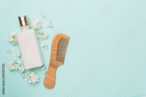 Shampoo with flowers and comb on color background  top view