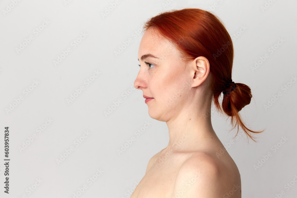 Portrait with young woman, girl with red hair standing over white studio background. Side view. Shot before plastic surgery. Chin correction