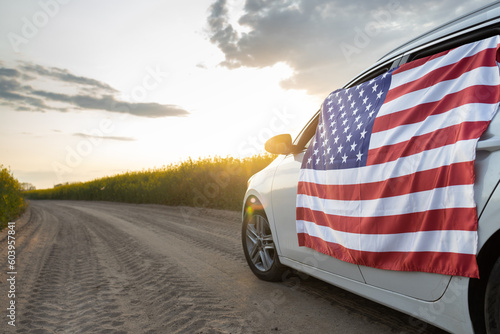 Foto large US flag is affixed to side of car driving down country road through rapeseed fields at sunset