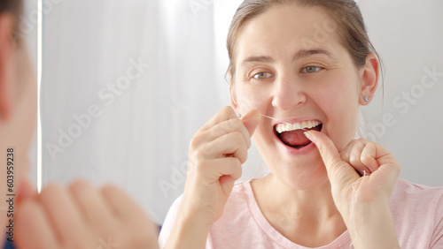 Closeup portrait of young woman using dental floss to clean her teeth. Concept of teeth health, self checking mouth and oral hygiene.