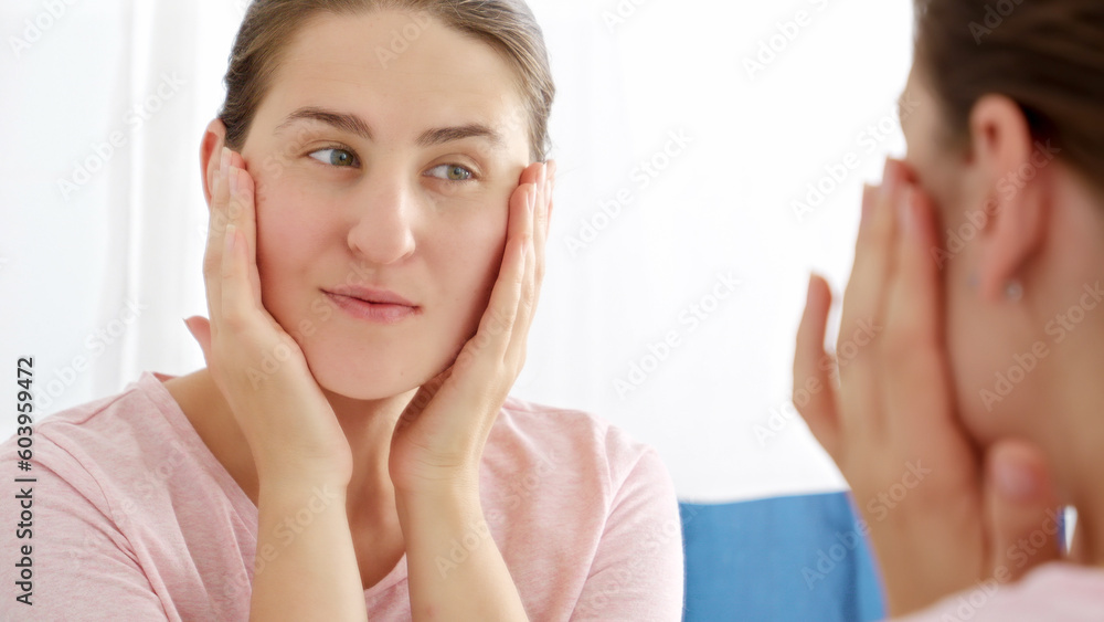 Beautiful smiling woman checking for wrinkles on her neck and massaging her face in bathroom. Concept of female aging, skin issues, facial treatment and care. Beautiful smiling woman checking for wrinkles on her neck and massaging her face in bathroom. Concept of female aging, skin issues, facial treatment and care.