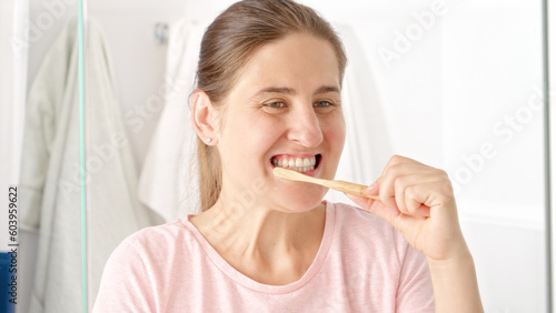 Beautiful young woman brushing her teeth at the mirror in bathroom. Concept of teeth health, self checking mouth and oral hygiene.