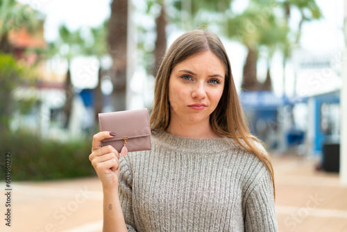 Young pretty blonde woman holding a wallet at outdoors with sad expression