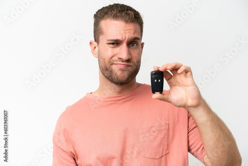 Young caucasian man holding car keys isolated on white background with sad expression