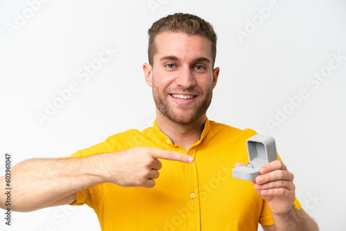 Young man holding a engagement ring isolated on white background and pointing it