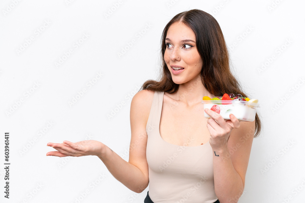 Young caucasian woman holding a bowl of fruit isolated on white background with surprise expression while looking side Young caucasian woman holding a bowl of fruit isolated on white background with surprise expression while looking side