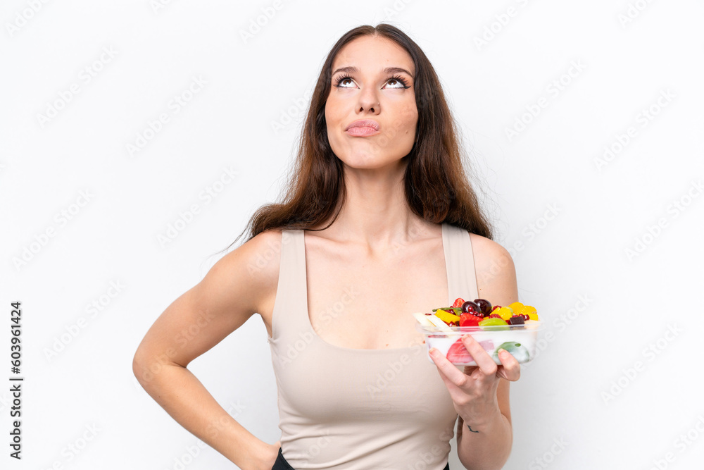 Young caucasian woman holding a bowl of fruit isolated on white background and looking up Young caucasian woman holding a bowl of fruit isolated on white background and looking up