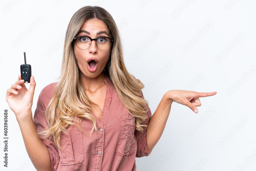 Young pretty Uruguayan woman holding car keys isolated on white background surprised and pointing side Young pretty Uruguayan woman holding car keys isolated on white background surprised and pointing side