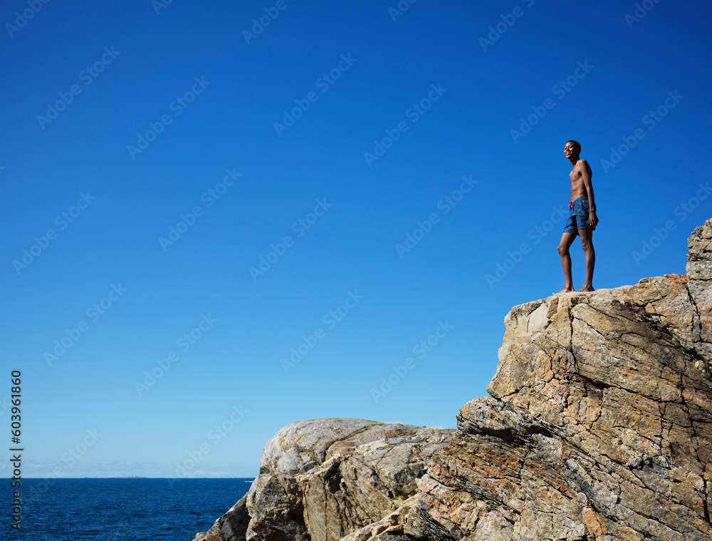 Young man standing on rock by sea Young man standing on rock by sea
