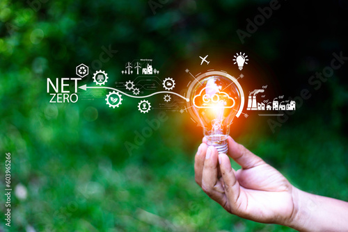 Net zero concept. Hand holding bulb with net zero icon. It is surrounded by a clean energy icon. Net zero 2050. Carbon gas affects global warming. Concept with innovation inspiration from big data.