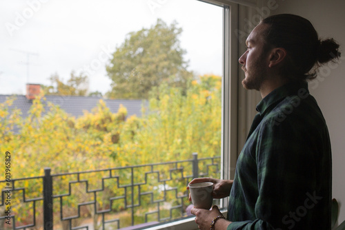 Young man with cup of coffee by window photo