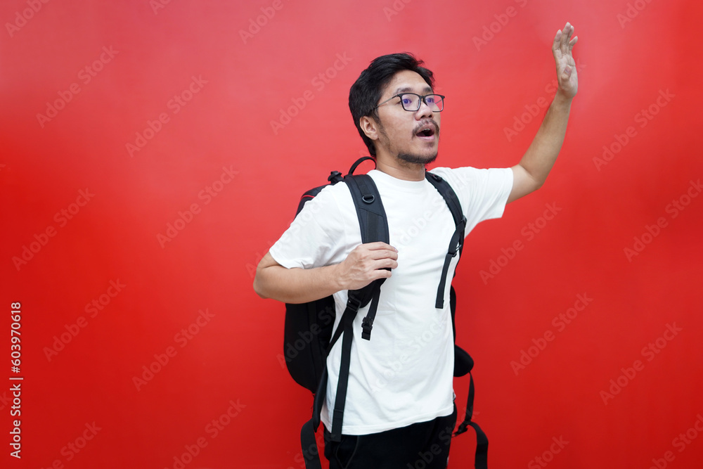 Φωτογραφία Portrait of young Asian tourist man raising hands carrying backpack ready to travel in studio isolated red background